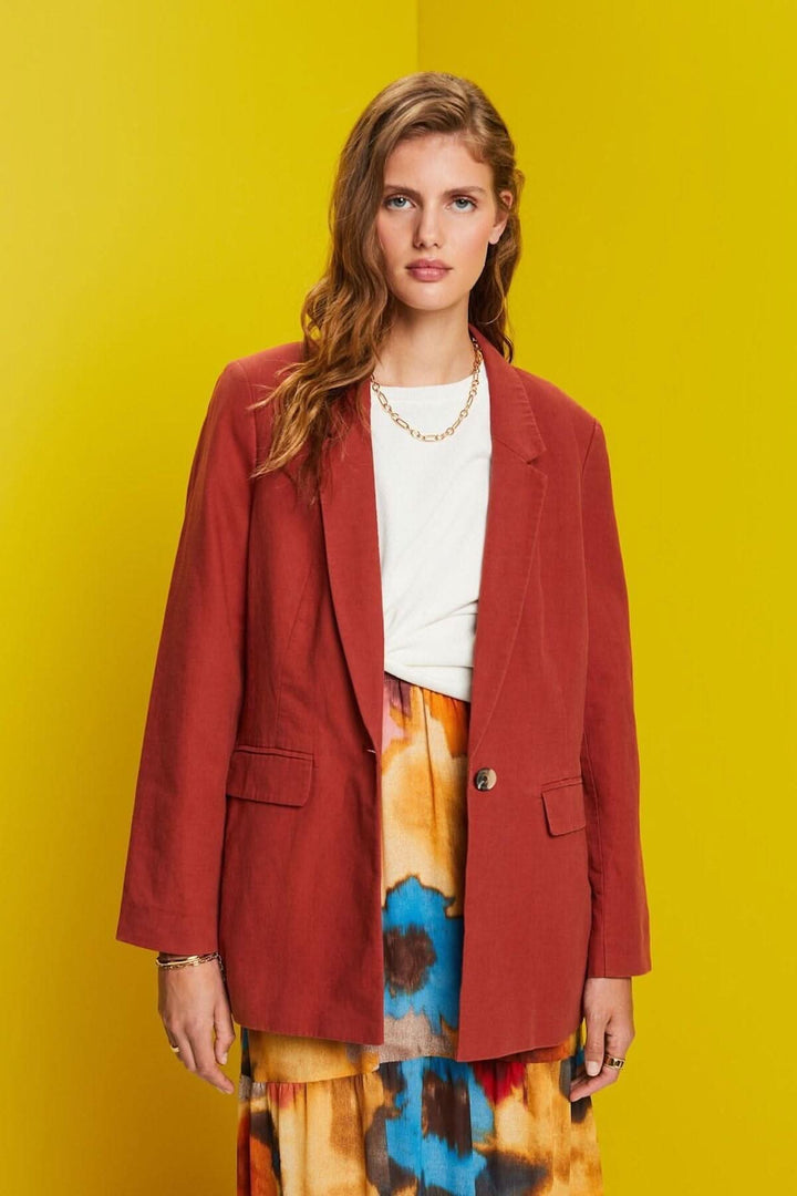 Blazer à simple boutonnage en lin, coupe droite, poches à rabat, porté sur fond jaune.