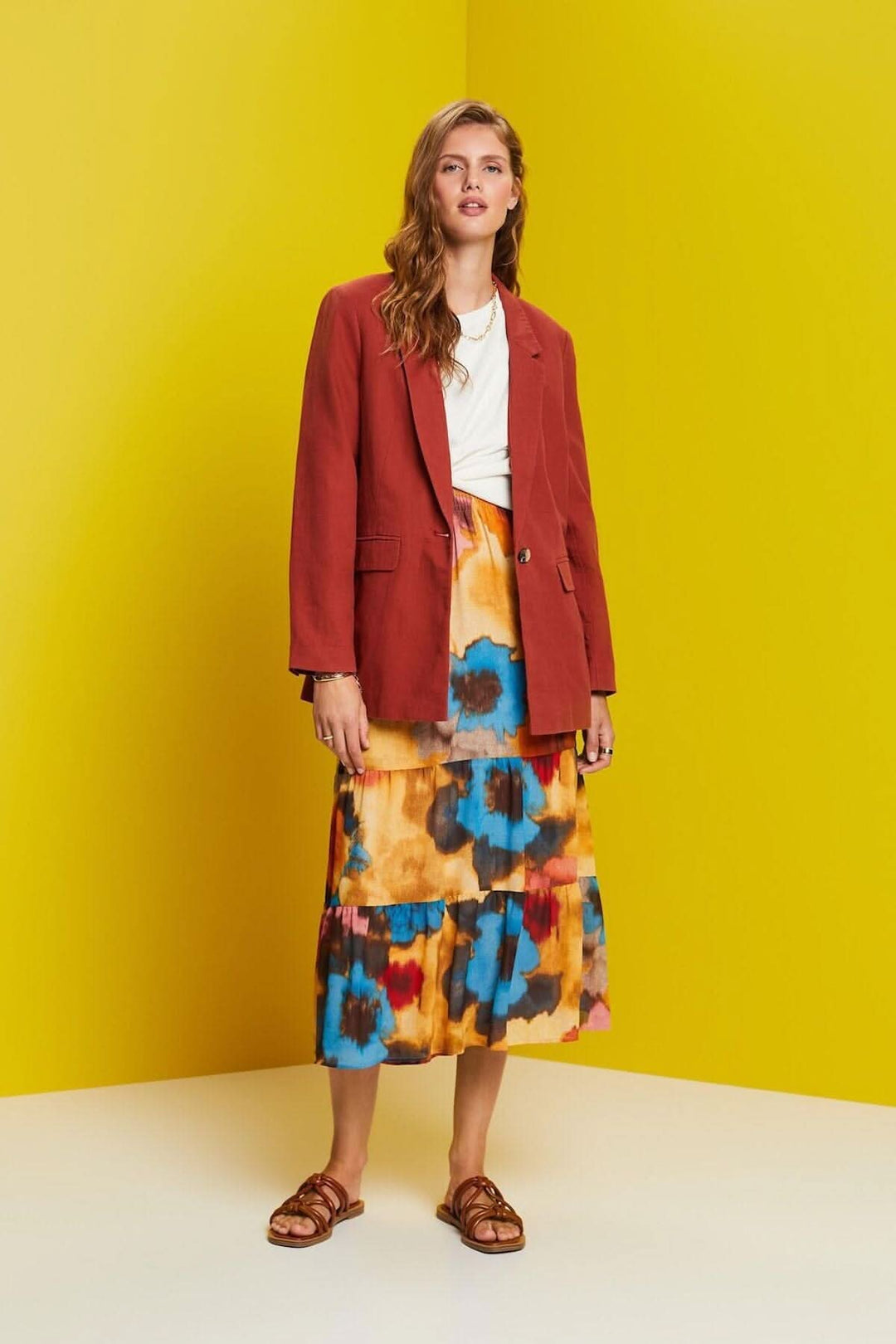 Femme portant un blazer à boutonnage simple rouge avec une jupe colorée, fond jaune.