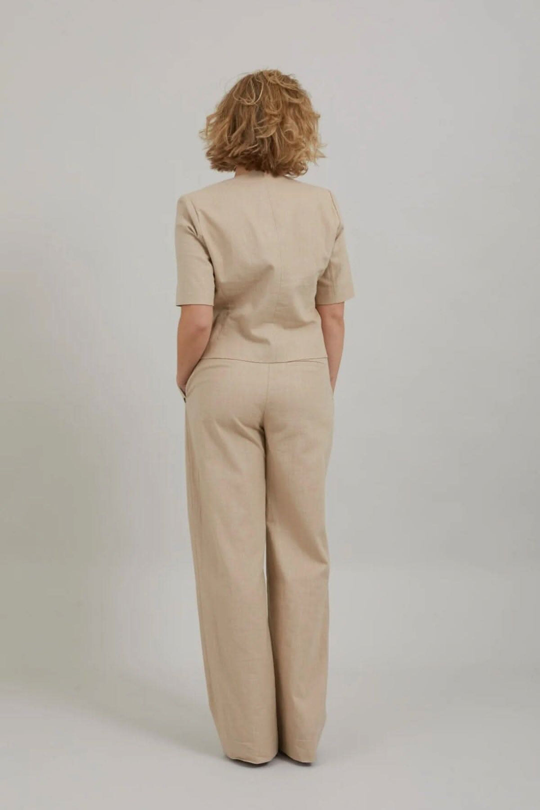 Femme de dos portant un ensemble beige chic avec manches courtes, parfait pour l'été et le bureau.