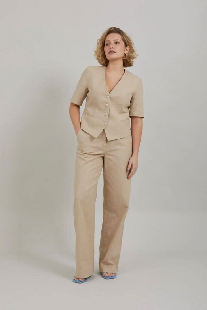 Modèle portant un blazer court beige à manches courtes avec pantalon assorti, style décontracté et chic.