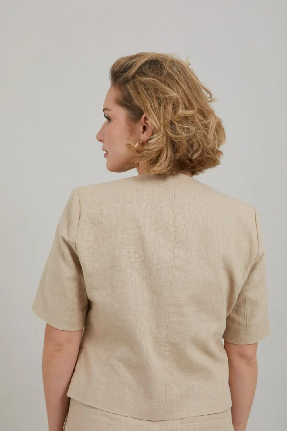 Femme vue de dos portant un blazer court beige à manches courtes, idéal pour l'été et le bureau.
