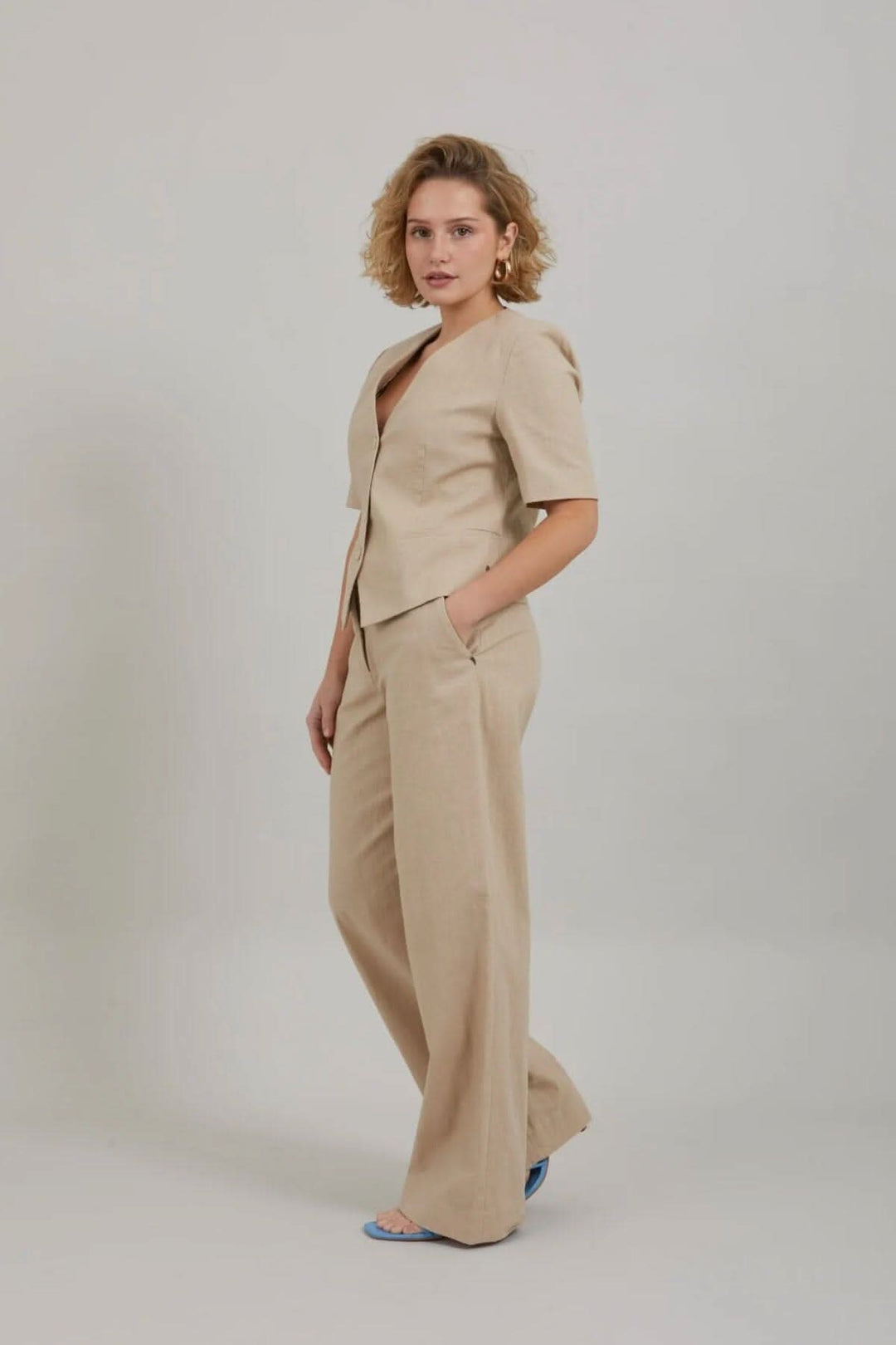 Femme portant un blazer court beige à manches courtes avec un pantalon assorti dans un style chic et décontracté.