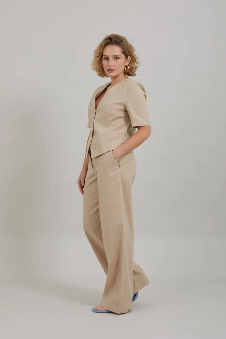 Femme portant un blazer court beige à manches courtes avec un pantalon assorti dans un style chic et décontracté.