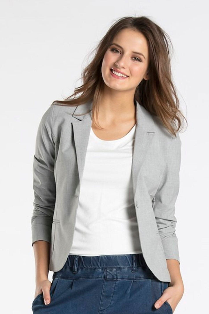 Femme souriante portant un blazer gris sur un t-shirt blanc, parfait pour des occasions professionnelles ou décontractées.