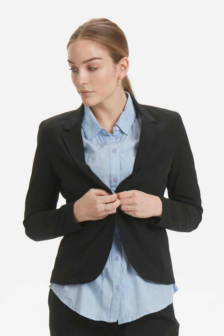 Femme portant un blazer Kajillian noir, avec une chemise bleu clair, prêt pour le bureau ou un événement.