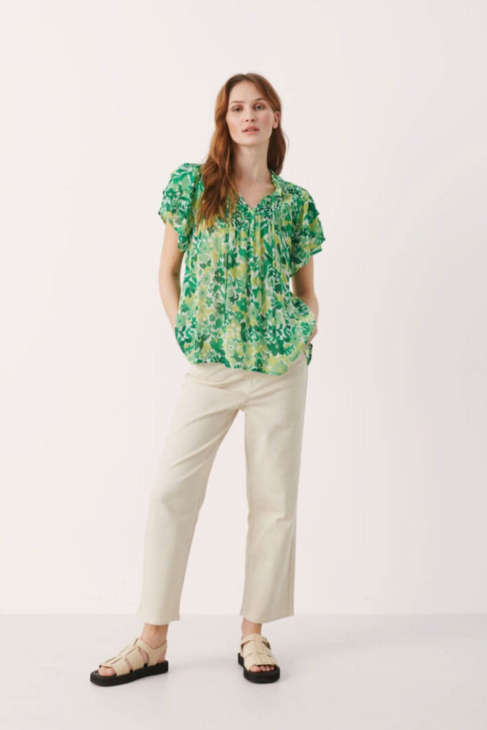 Blouse fleurie Sinna, légère et fluide, portée avec un pantalon crème, affichant un joli imprimé vert.