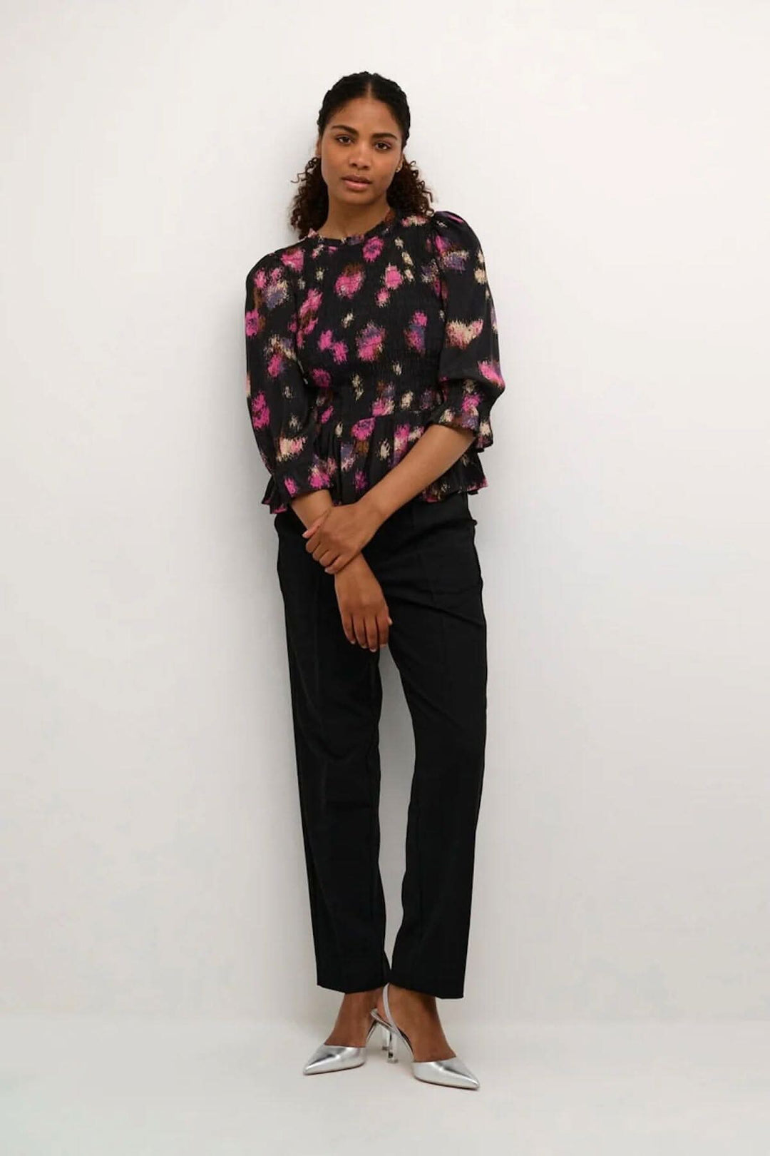 Femme portant une blouse noire à imprimé floral rose fuchsia, avec un style ajusté et manches amples.