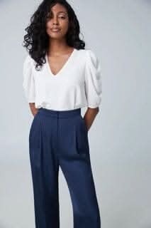 Blouse à manches courtes gigots avec col en V, portée avec un pantalon bleu marine, élégante et polyvalente.