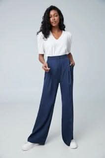 Femme portant un haut blanc et un pantalon large bleu marine, posant sur fond neutre.