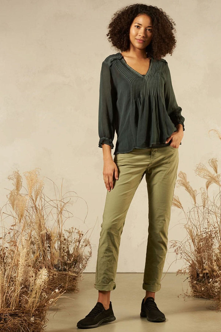 Blouse avec col en V, détails de couture, style décontracté, portée par mannequin sur fond naturel.