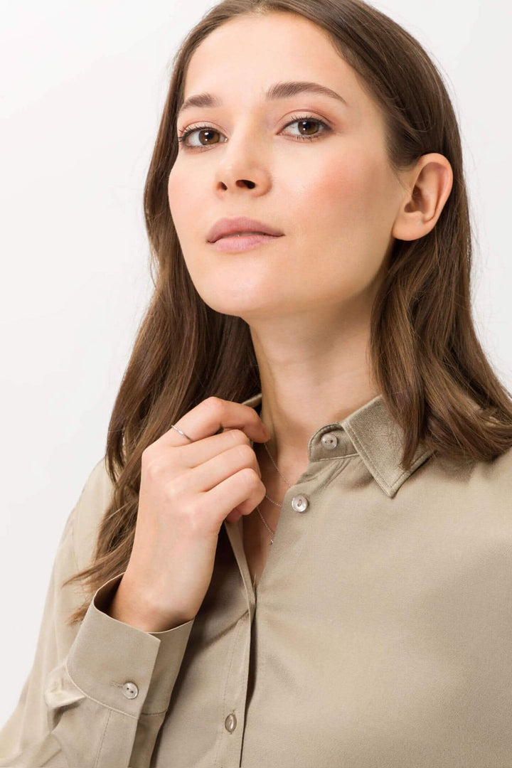 Femme en chemisier beige à col chemise, manches longues, patte de boutonnage, look élégant.