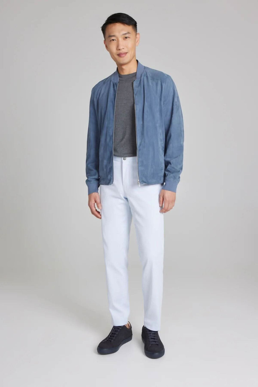 Homme portant un bomber ultraléger en daim bleu, t-shirt gris et pantalon blanc, prêt pour un look élégant.