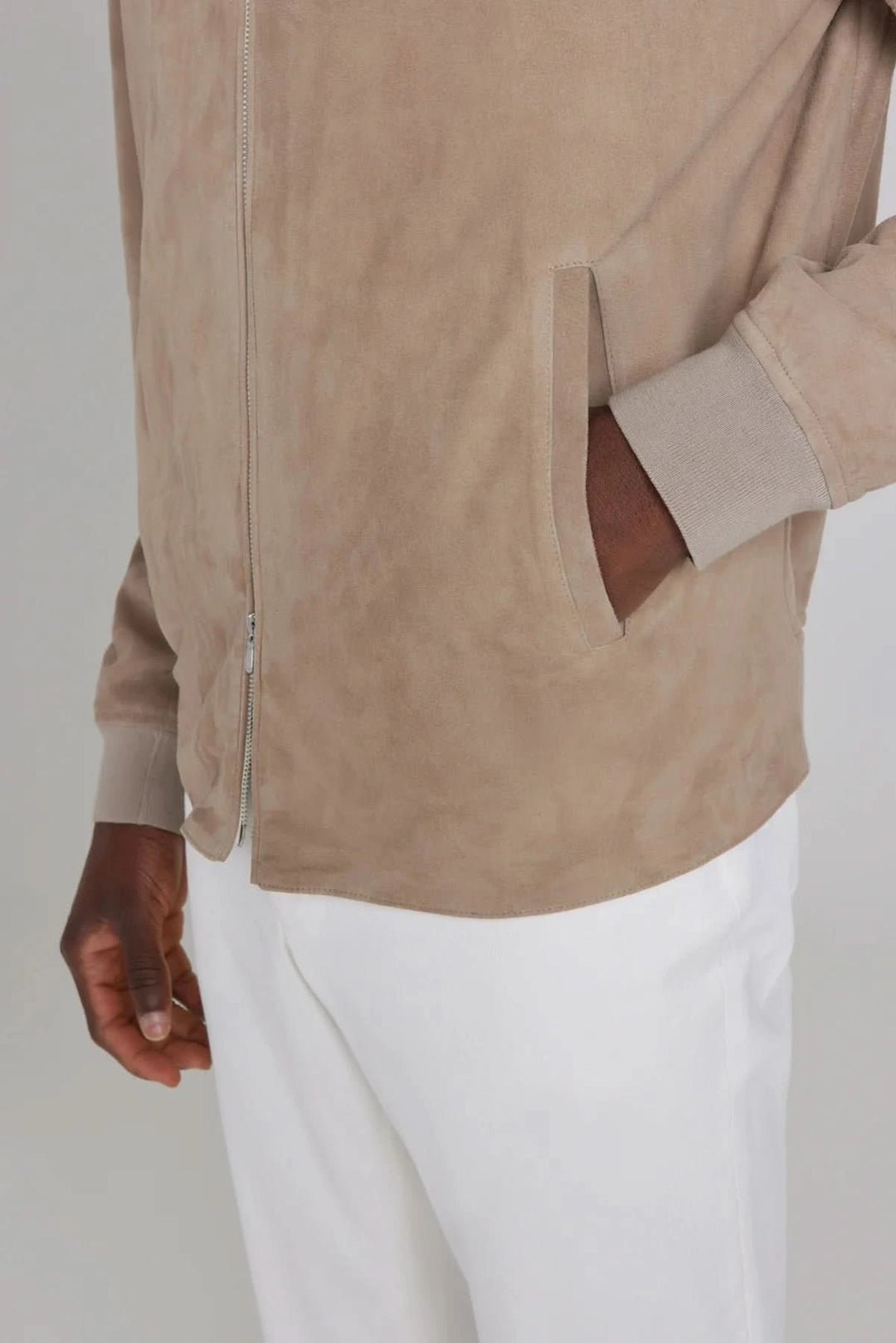 Détails du bomber ultraléger en daim, couleur beige, avec poches latérales, porté avec un pantalon blanc.