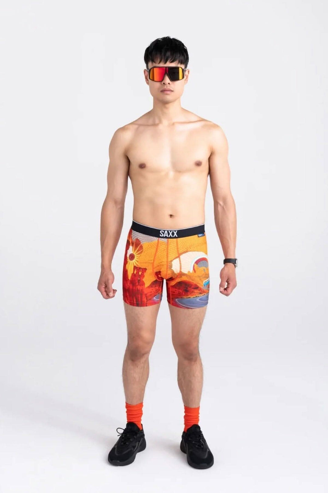 Homme portant des boxers SAXX avec un design inspiré des parcs nationaux, lunettes de soleil et chaussettes orange.