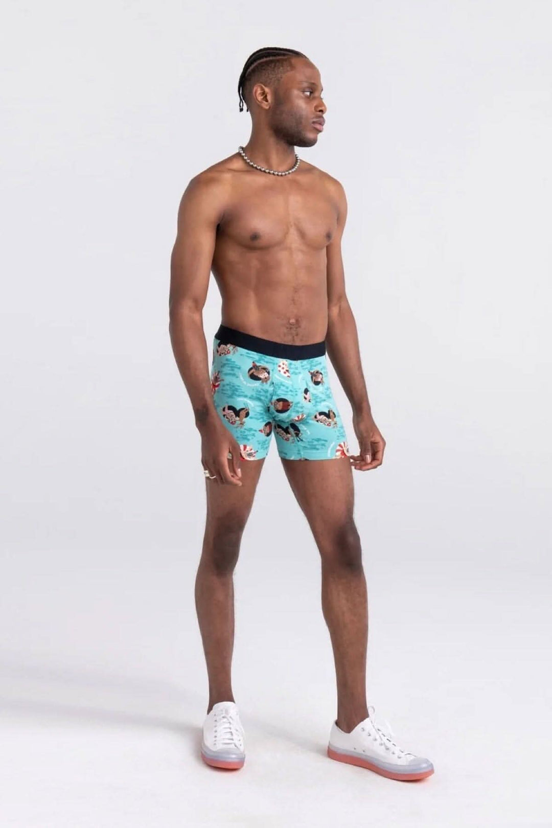 Homme en maillot de bain boxer à motifs colorés, posé sur fond neutre, affichant un look décontracté.