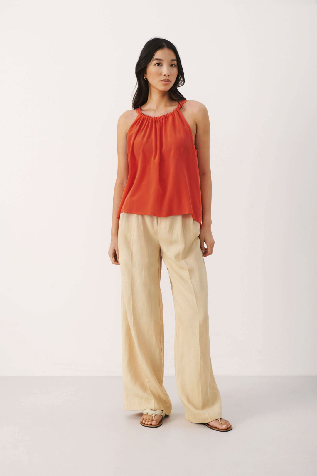 Camisole Arine rouge avec col rond, portée par un mannequin, complétée par un pantalon beige léger.