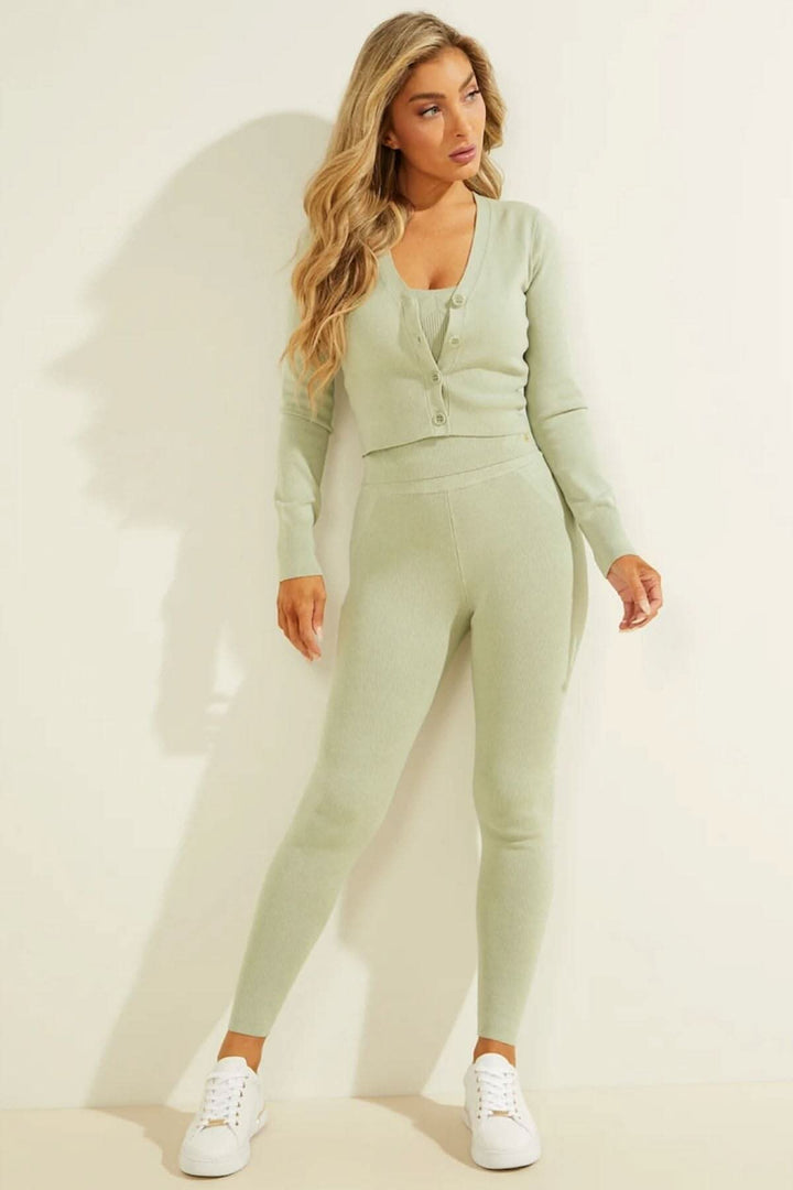 Femme portant un cardigan Briana en tricot vert avec leggings assortis et baskets blanches sur fond neutre.