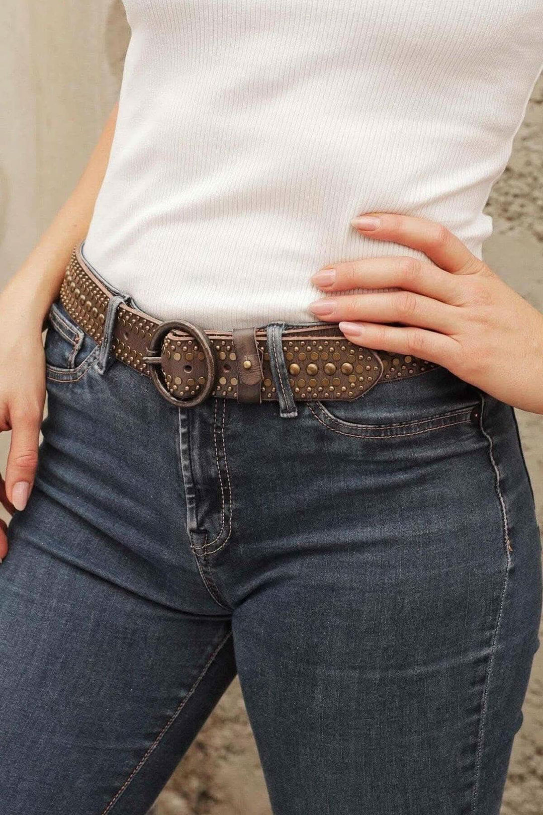 Ceinture en cuir cloutée avec clous en bronze, portée avec un haut blanc et un jean.