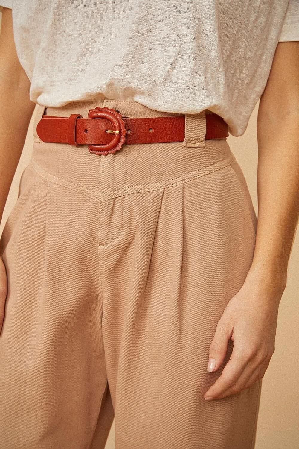 Ceinture Marguerite en cuir acajou avec boucle festonnée, portée sur un pantalon beige. Accessoire de mode élégant.
