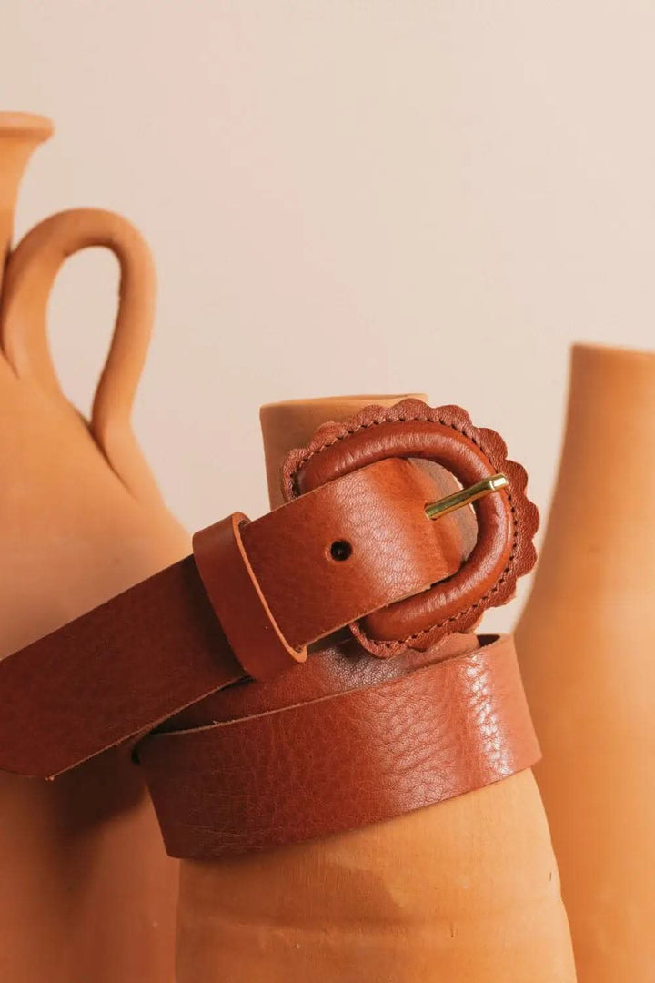 Ceinture Marguerite en cuir acajou avec boucle festonnée, présentée à côté de pots en terre cuite.