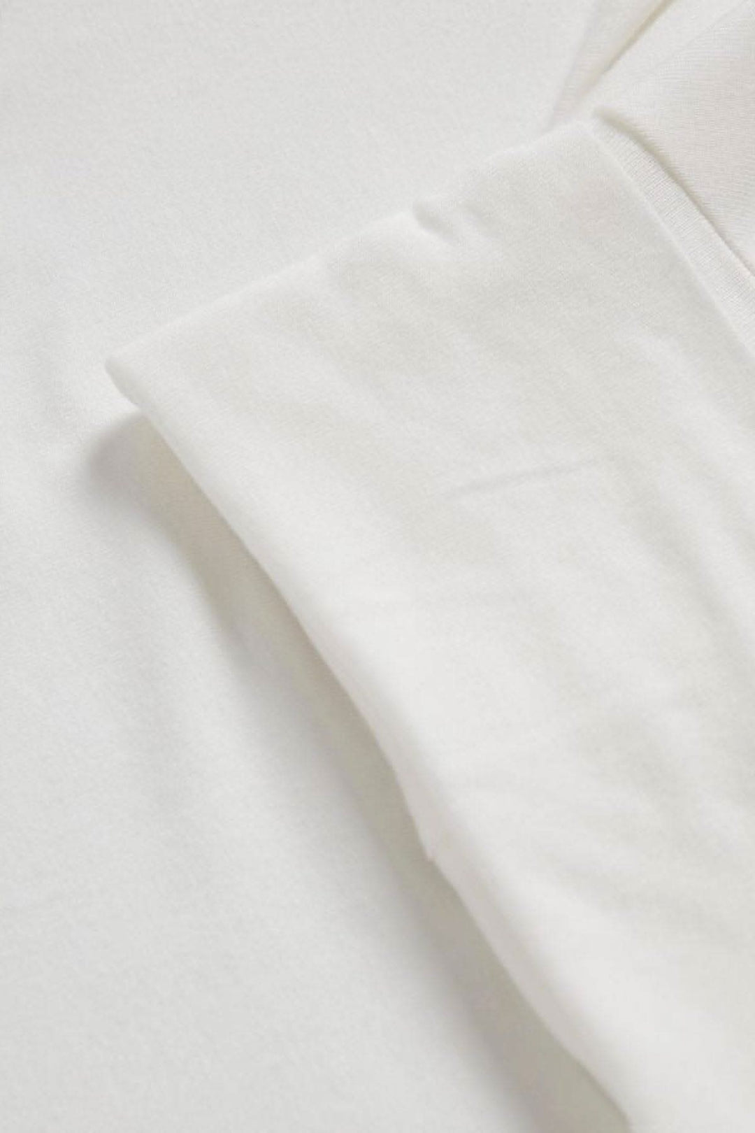Détail d'un chandail à col roulé blanc en viscose et élasthanne, montrant la texture douce et la couture des manches.