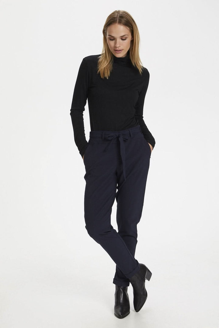 Chandail à col roulé manche longue noir, associé à un pantalon en tissu fluide, style décontracté.