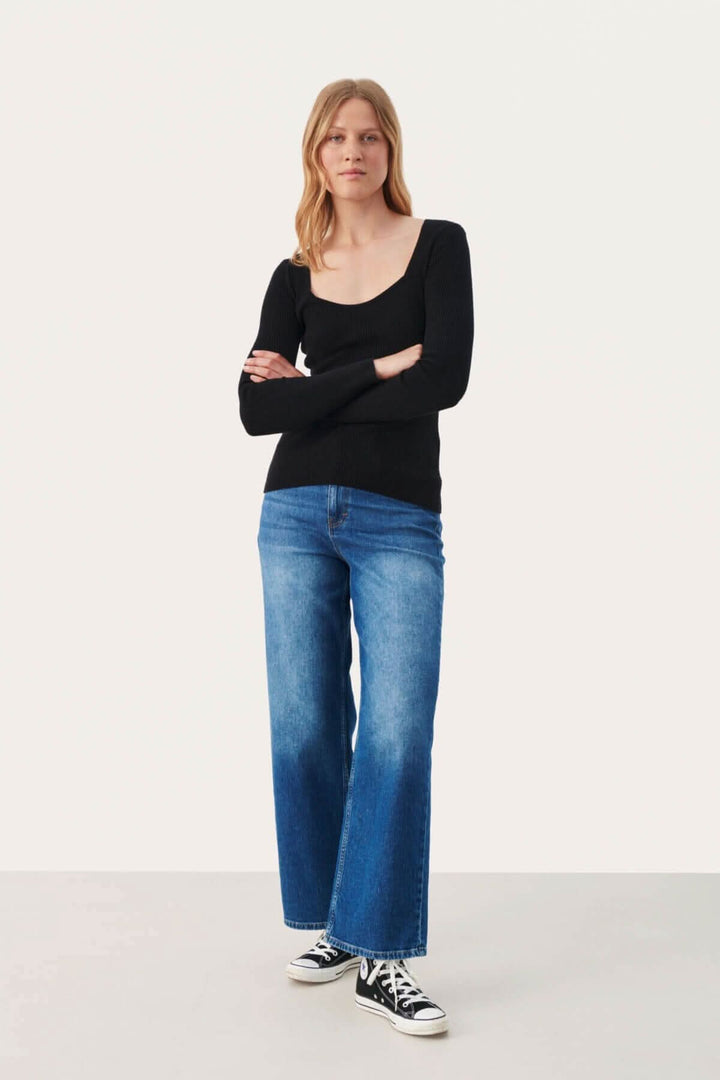 Modèle portant le pull Caylee noir à col profond avec jeans larges, parfait pour un look décontracté et moderne.
