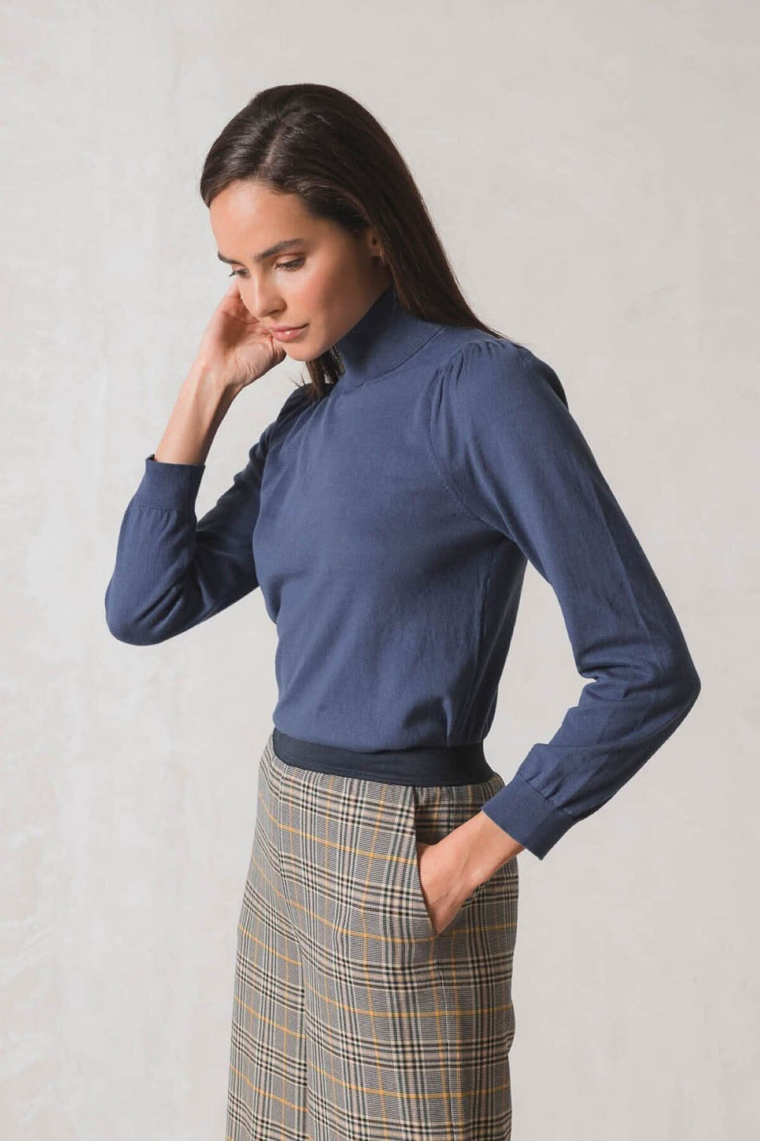 Femme portant un chandail col roulé bleu, manches longues, et jupe à carreaux, style élégant et moderne.