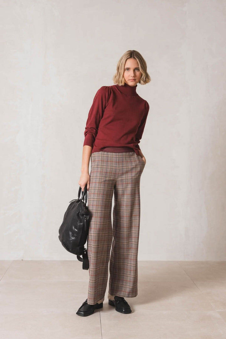 Femme portant un chandail col roulé bordeaux avec un pantalon à carreaux, sac noir à la main.