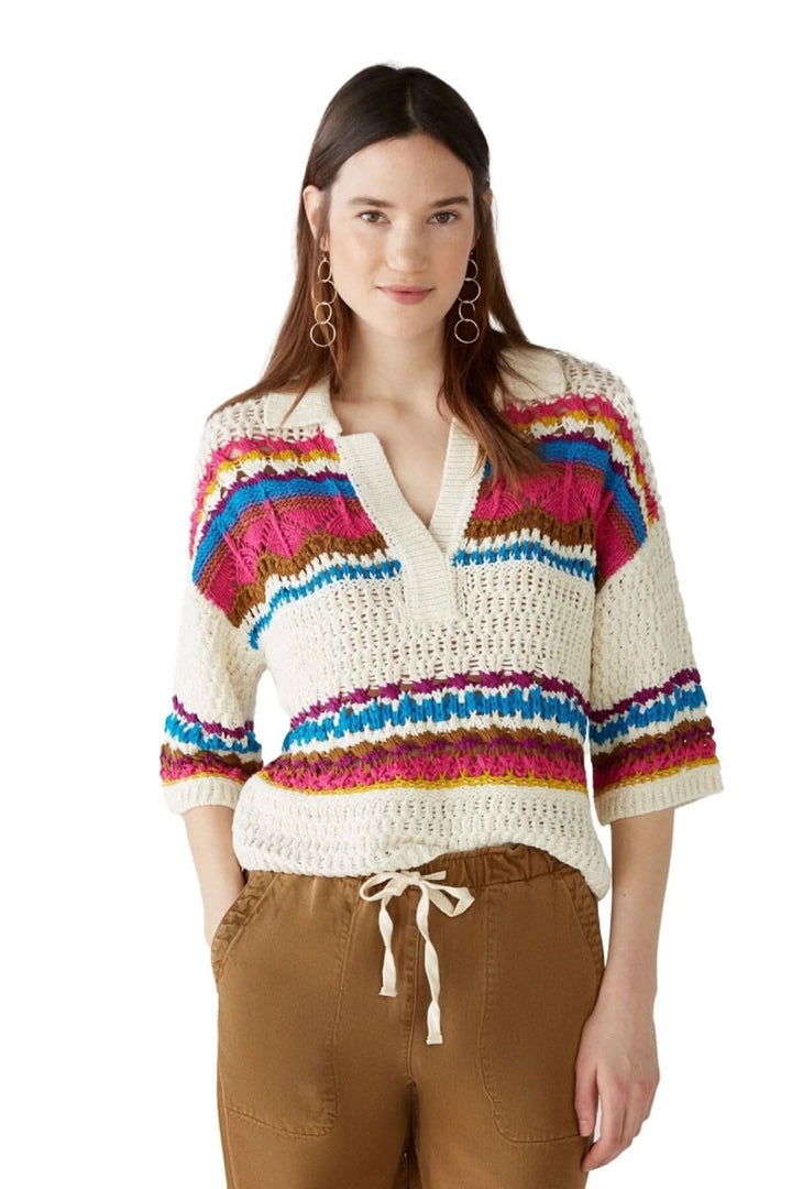 Chandail en tricot avec motifs abstraits, encolure en V, manches courtes, porté avec un pantalon beige.