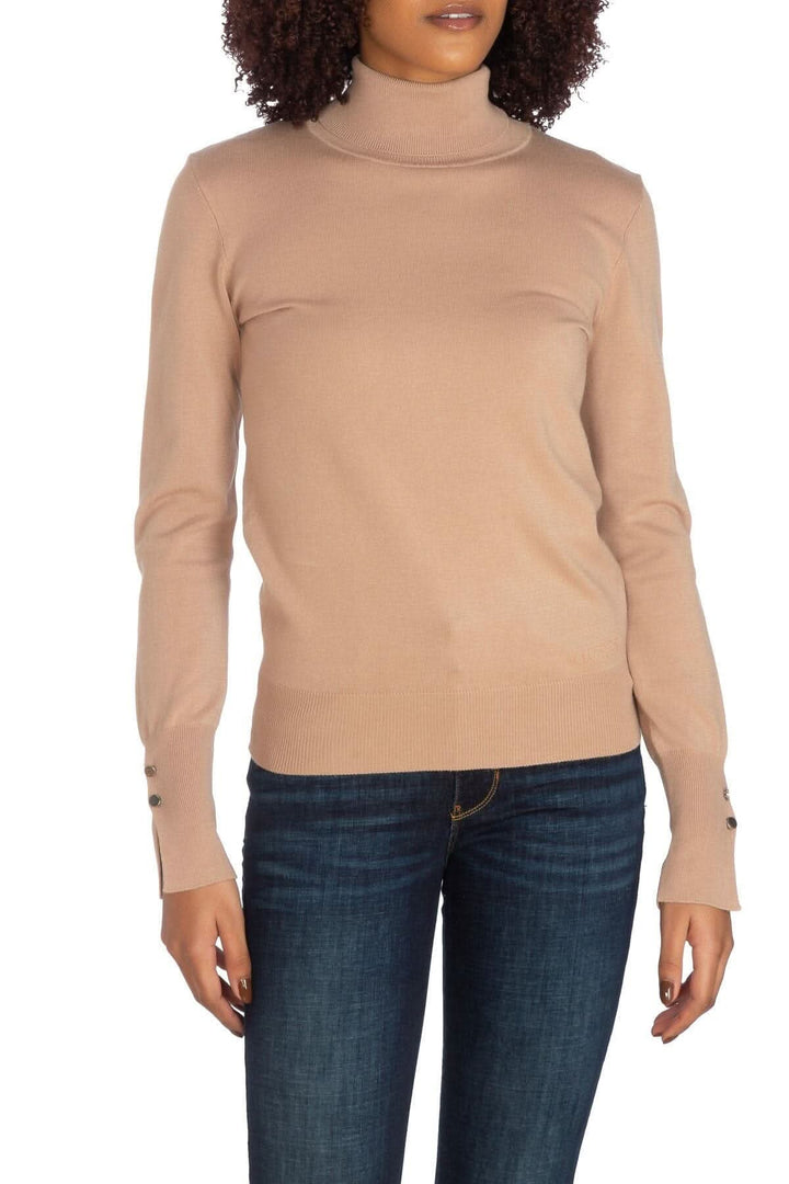 Chandail beige à col roulé, doux et élastique avec boutons aux manches, porté avec un jean.