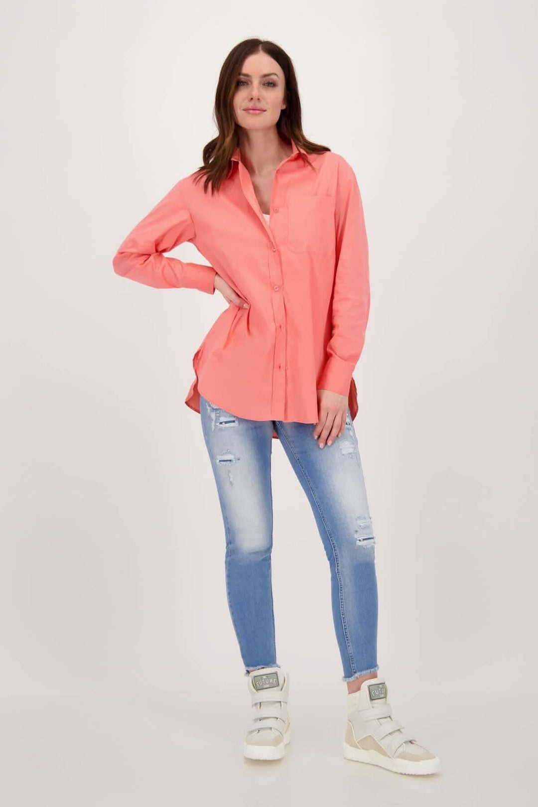 Femme portant une chemise en coton rose avec jeans déchirés et baskets blanches, style décontracté et moderne.