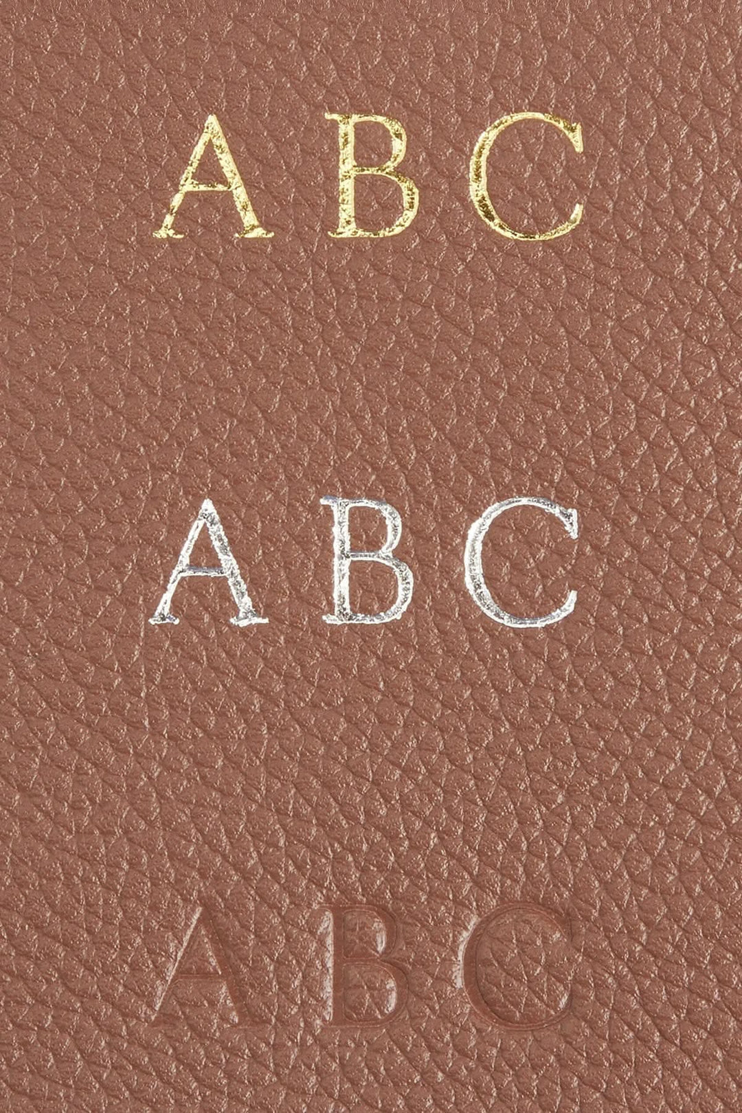 Détails de monogrammes personnalisés en cuir sur un classeur à anneaux, incluant lettres dorées, argentées et en relief.