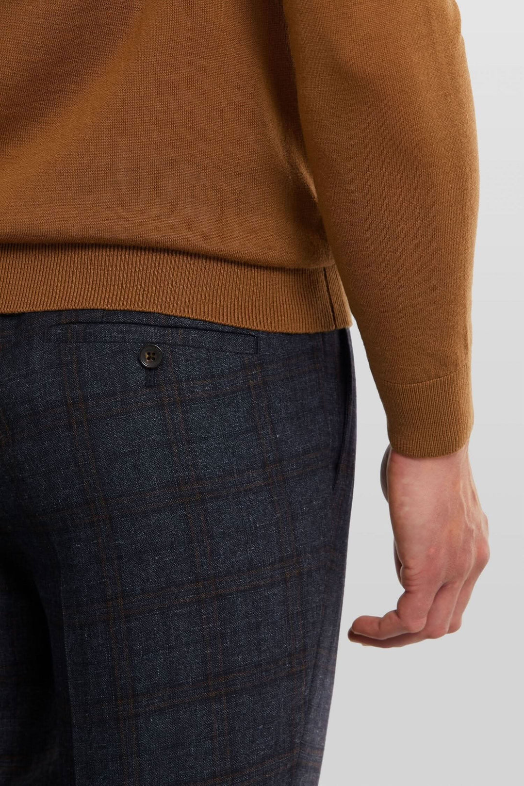 Détail d'un col roulé en laine brun cacao avec un pantalon à motif carreaux bleu foncé.