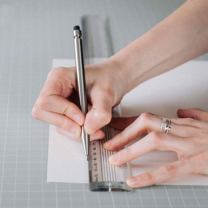 Une main utilisant un crayon Modern Fuel sur une règle pour dessiner sur du papier blanc.