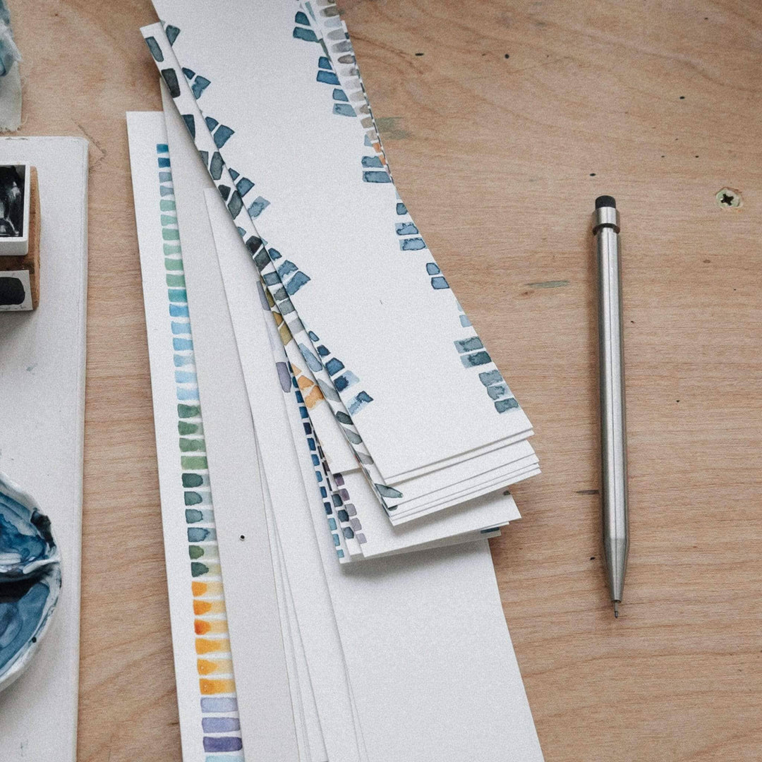 Échantillons de couleurs et croquis sur une table en bois, avec un crayon en métal à côté.