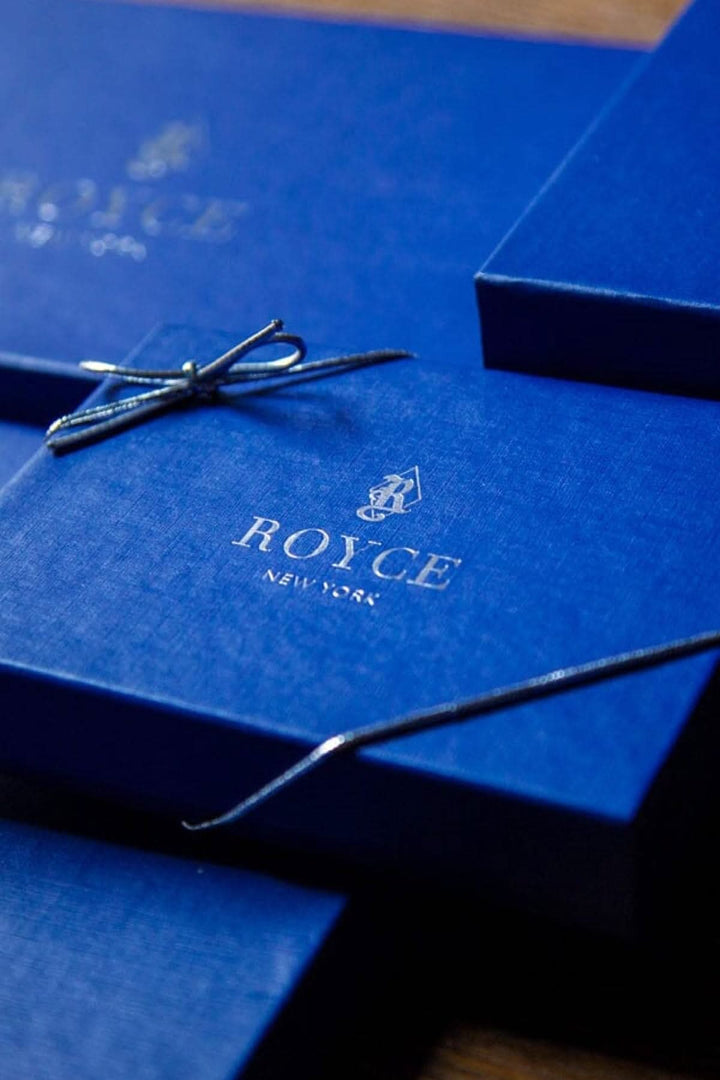 Boîtes bleu royal de la marque ROYCE, élégamment emballées avec un nœud en satin, parfaites pour des cadeaux uniques.