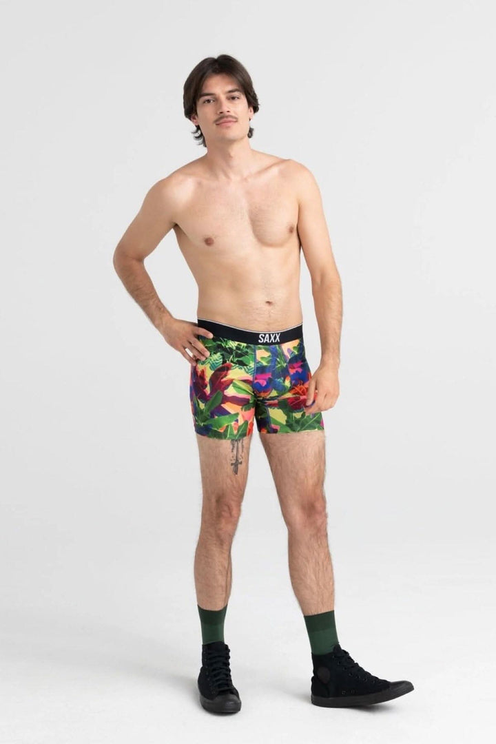 Homme portant des boxers colorés avec motif feuillage lumineux, debout sur fond neutre.