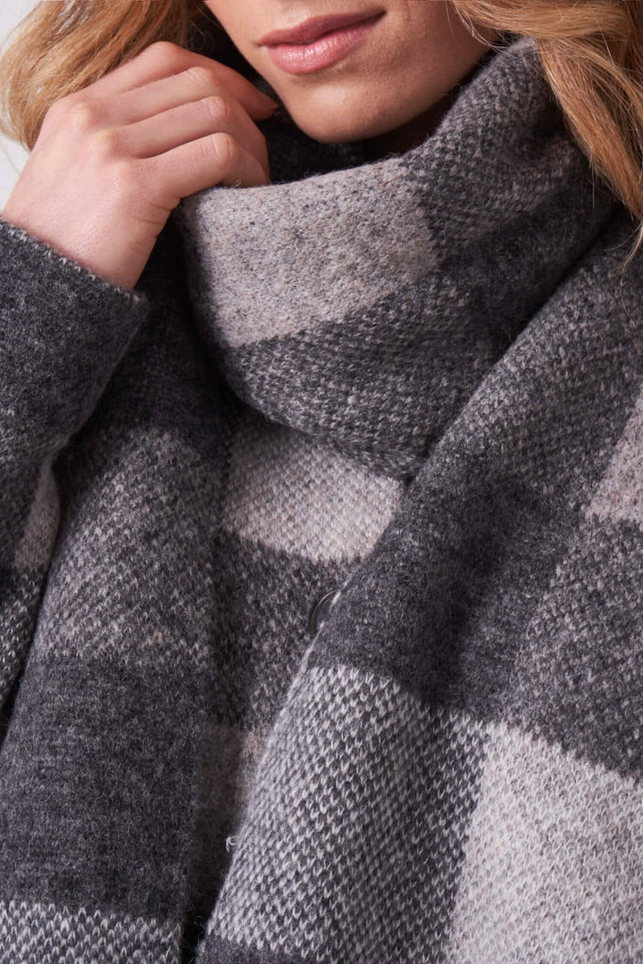 Foulard à carreaux gris et beige, long et avec franges, porté autour du cou.
