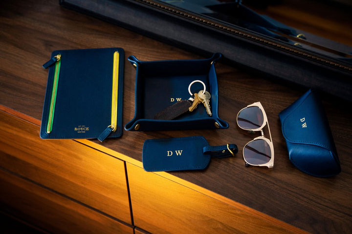 Handcrafted leather luggage tag with gold tone hardware, personalized with initials, alongside accessories on wooden surface.