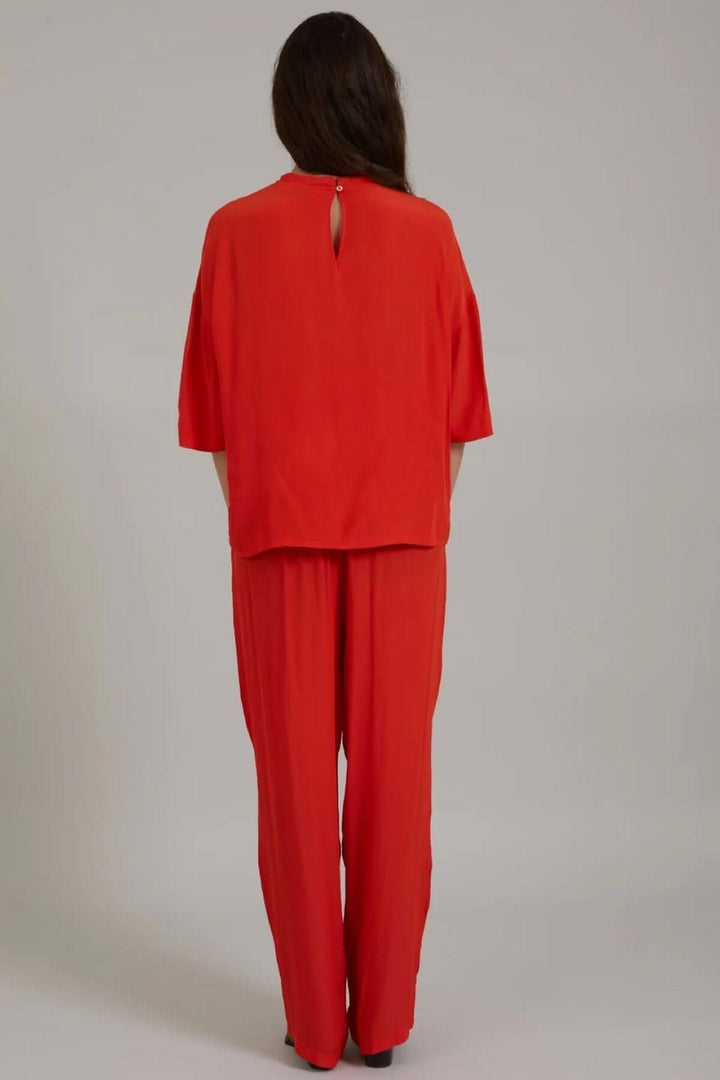 Haut rouge à manches midi avec ouverture à boutons, porté avec un pantalon assorti, vue arrière.