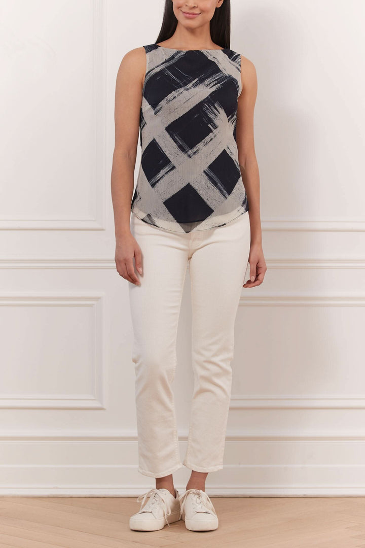 Top sans manches imprimé à motif géométrique, porté avec un pantalon blanc et des chaussures décontractées.