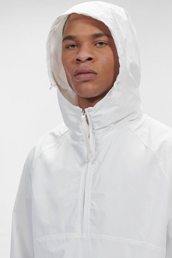 Homme portant un sweat-shirt à capuche blanc avec demi-fermeture zippée et tissu mat résistant à l'eau.