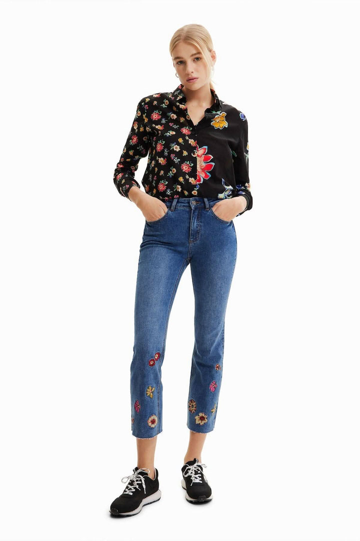 Femme portant un jean court évasé avec broderie florale, associé à une chemise à motifs.