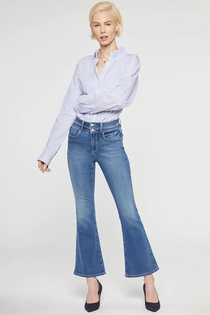 Modèle portant le jean évasé Ava de NYDJ, taille haute, en denim bleu, avec une chemise claire et des talons.