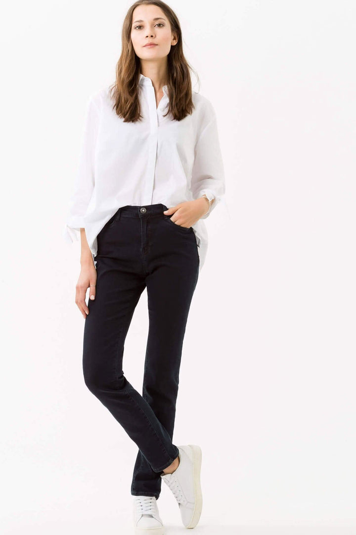 Femme portant le jean Mary de BRAX, avec chemise blanche et baskets, style décontracté et moderne.