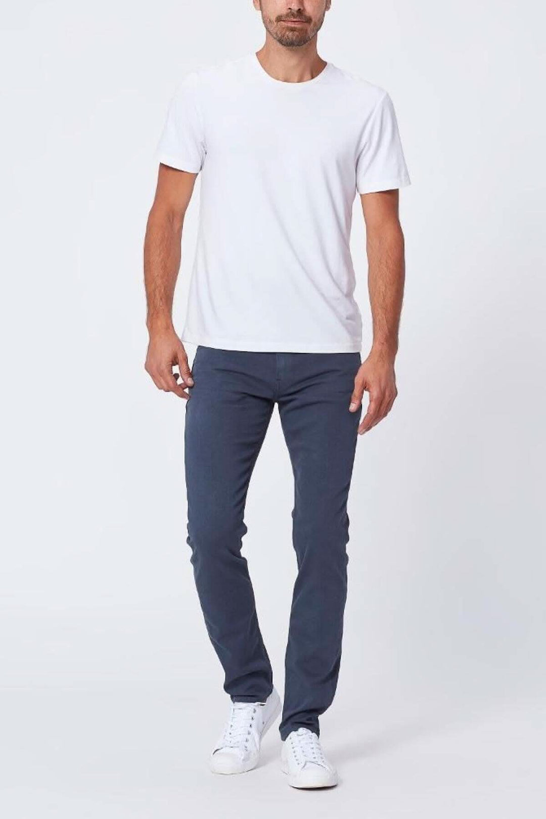 Homme portant un t-shirt blanc et un pantalon slim bleu, avec des chaussures blanches.