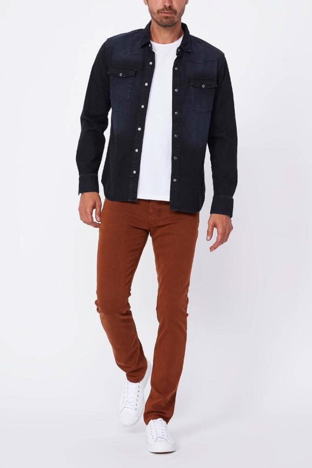 Homme en chemise en denim noir et pantalon russet, portant des sneakers blanches, posant sur fond blanc.