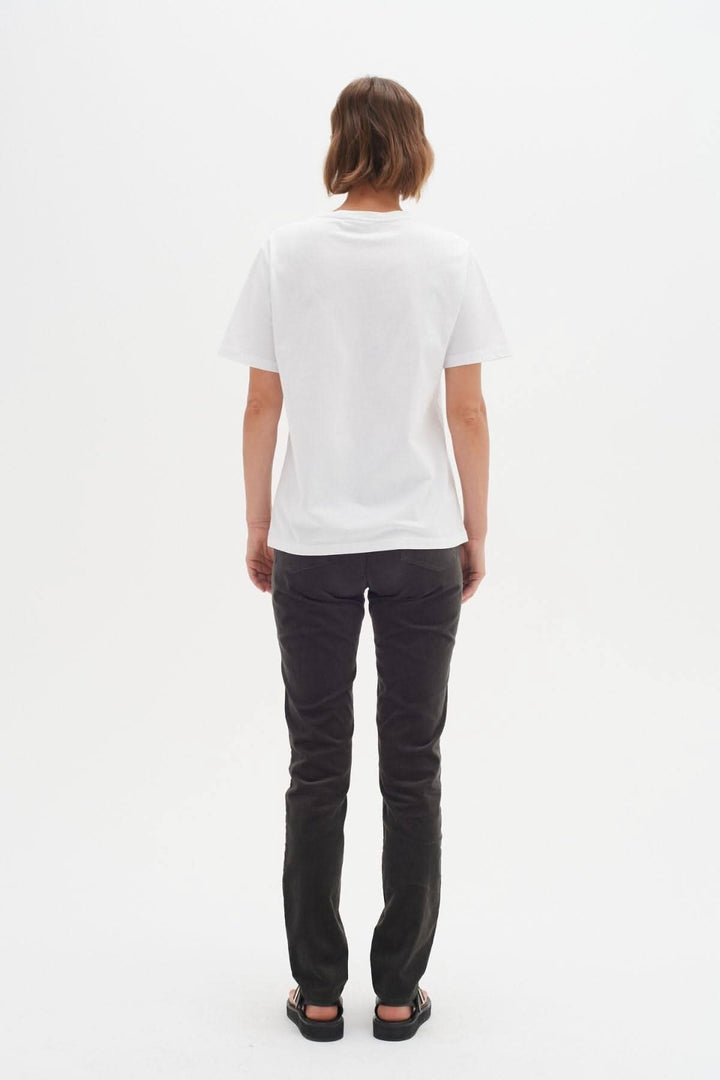 Femme vue de dos portant un t-shirt blanc et un jean foncé, sur fond blanc.