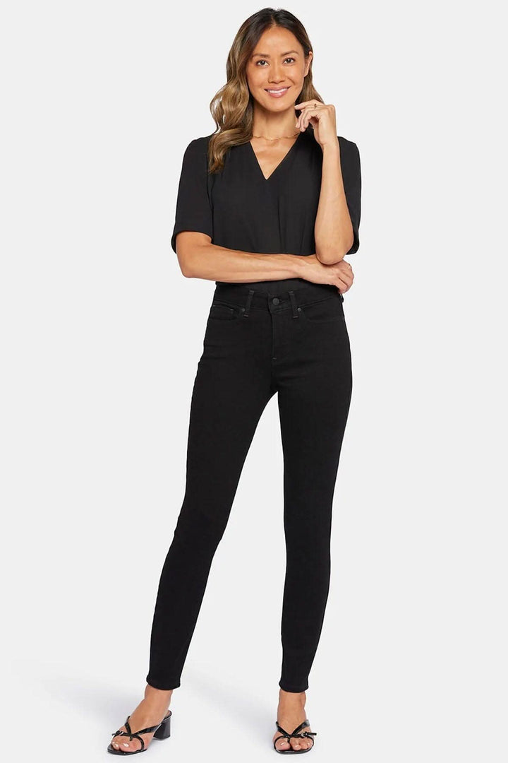 Femme en jean skinny noir avec top noir, affichant un look chic et moderne.